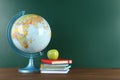 Globe, books and apple on wooden table near green chalkboard, space for text. Geography lesson Royalty Free Stock Photo