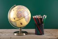 A globe in front of the blackboard and a pen holder filled with colored pencils