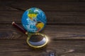 Globe and magnifier, wooden background.