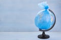 Globe of planet Earth dressed in a garbage plastic bag on blue wooden background