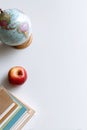 globe sits next to bright red apple and stack of notebooks on white table. This setup reflects quiet study area, perfect for Royalty Free Stock Photo