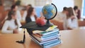 A globe of the world with textbooks and a college graduate& x27;s cap in a school classroom during class.