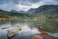 Gloomy Lake Raduzhnoe in front of rocks among the taiga and large stones under storm clouds in Ergaki