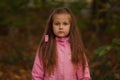 Gloomy long-haired girl child in pink jacket in the woods