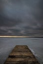 gloomy severe winter vertical gray landscape. an old wooden boardwalk pier on a large frozen lake under a thick dramatic cloudy Royalty Free Stock Photo