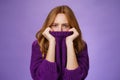 Gloomy upset redhead girlfriend pulling collar of purple sweater on nose, frowning and squinting offended, being