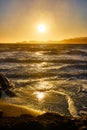 Glorious golden sunset over ocean waves rolling into sandy shore with distant mountains Royalty Free Stock Photo