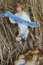 Vintage angel figure looks down on baby Jesus in the manger. Macro image has straw background.