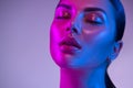 Glossy, wet skin makeup. Fashion model woman face in bright neon colourful lights, beautiful woman, UV, ultraviolet trendy make-up