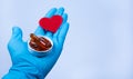 Gloved doctorÃ¢â¬â¢s hand holding red heart symbol and box with omega capsules on blue background. Heart diseases