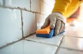 Gloved hand cleans tile seams with sponge. White ceramic wall tiles get cleaned with cleaning tool. Routine home upkeep task, Royalty Free Stock Photo