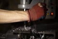 Gloved hand drills part. Worker`s hand in garage. Red glove with hole