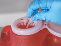 Gloved hand dropping a used needle into a bright red sharps container Royalty Free Stock Photo