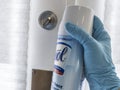 Gloved hand holding a spray cannister of Lysol, aimed at a door handle indoors