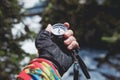 A gloved hand holds a magnetic compass against the background of a coniferous forest and mountain river. The concept of