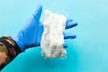 Gloved hand holds medical mask over blue background.