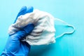 Gloved hand holds medical mask over blue background.