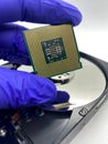 Gloved hand keeping a microprocessor CPU chip closeup against a silver hard disk plate