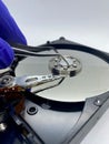 Gloved hand keeping a pincer on silver hard disk plate closeup view with selective focus on foreground Royalty Free Stock Photo