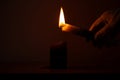 Gloved hand lighting a candle from another candle in the dark against a warm soft light Royalty Free Stock Photo