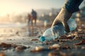 A gloved hand picks up a plastic bottle from a polluted beach with people in the background Royalty Free Stock Photo