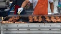 Gloved hand turning meat grilling on large BBQ