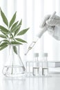 A gloved hand uses a dropper with liquid over a flask with a plant and test tubes in a clean laboratory setting. Royalty Free Stock Photo
