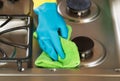 Gloved hand wiping down stove top range with green microfiber ra