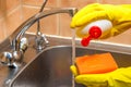 gloved hands with dishwashing liquid and a sponge in the kitchen