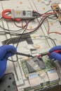 Gloved hands of an electrician engineer hold multimeter probe. Repair and diagnostics of printed circuit board of TV in service