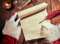 Gloved hands of Father Christmas writing on a vintage parchment scroll with a feather quill pen by candlelight with copy space on