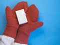 Gloved hands, mittens with a Christmas gift, a white gift box on a blue background. New Year, winter birthday