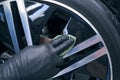 Gloved worker applies wax to automobile wheel, tire close-up. Car care