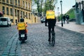 Glovo courier service. Two food deliverymen with Yellow backpacks on a motorbike on a bicycle ride along a city street