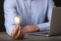 Glow up your ideas. Closeup view of man holding light bulb while working at wooden desk, space for text Royalty Free Stock Photo