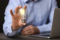 Glow up your ideas. Closeup view of man holding light bulb while working at wooden desk, space for text Royalty Free Stock Photo