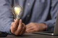 Glow up your ideas. Closeup view of man holding light bulb while working at wooden desk, space for text Royalty Free Stock Photo