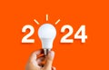 Glowing 2024 calendar year numbers, neon style with creative trend light bulb holding by businessman's hand.