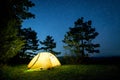 Glowing camping tent in the night mountain forest under a starry sky