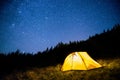 Glowing camping tent in the night mountain forest under a starry sky