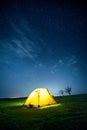 Glowing camping tent in the night mountains under a starry sky