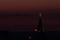 Glowing cross on the spire of a Babtist church at dusk against a sunset crimson sky over the horizon in the city of Syktyvkar in Royalty Free Stock Photo