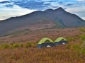 Glowing Green tents in the mountains under dramatic evening sky. Red sunset and mountains in the background.