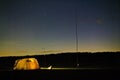 Glowing illuminated camping tent in the field among the forest. Dog seating near the tent, radio antenna. Summer night