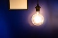 Glowing light bulb against blue wall. Royalty Free Stock Photo