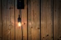 Glowing light bulb hanging near wooden panaled wall background texture, modern interior decoration, copy space for text Royalty Free Stock Photo