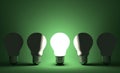 Glowing light bulb in row of switched off ones on green. Front view Royalty Free Stock Photo