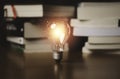 Glowing lightbulb in front of heap of books for education of creative thinking innovation idea and problem solving concept