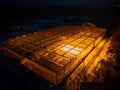 Glowing modern glass greenhouse in winter night, aerial view