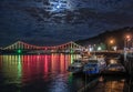 Glowing multicoloured city bridge above river and boats at quay Royalty Free Stock Photo